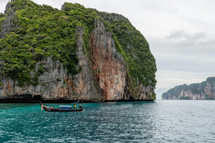 A longtail boat navigating the stunning limestone cliffs of Phuket, Thailand's vibrant ocean landscape.