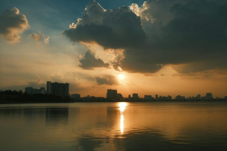 Dramatic sunset over city skyline with reflections on water, creating a warm and serene atmosphere.