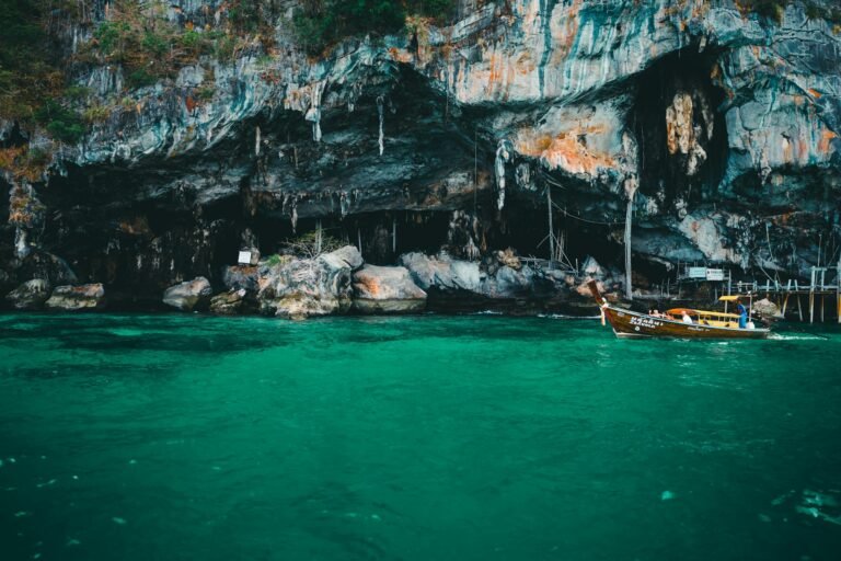 Scenic view of a longtail boat by limestone cliffs in the turquoise waters of Phuket, Thailand.