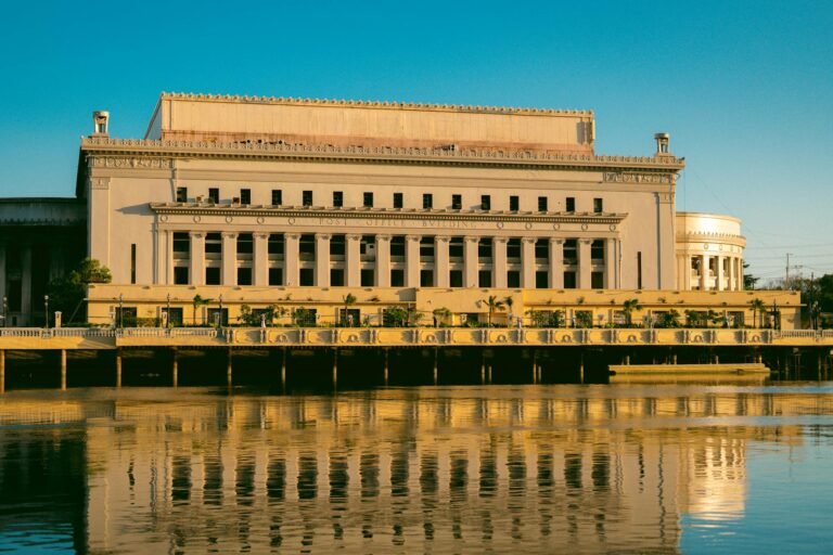 Capture of the iconic Manila Post Office, reflecting in the tranquil Pasig River under a clear sky.