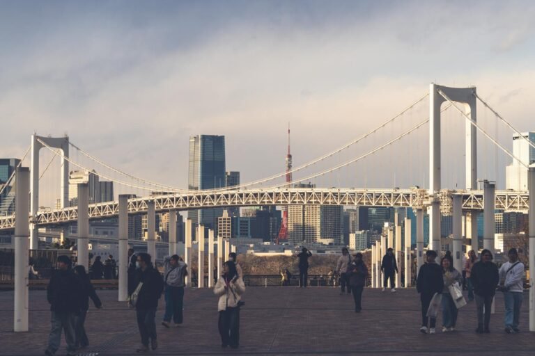 Beautiful sunset view of Rainbow Bridge and Tokyo skyline with people strolling on a promenade.