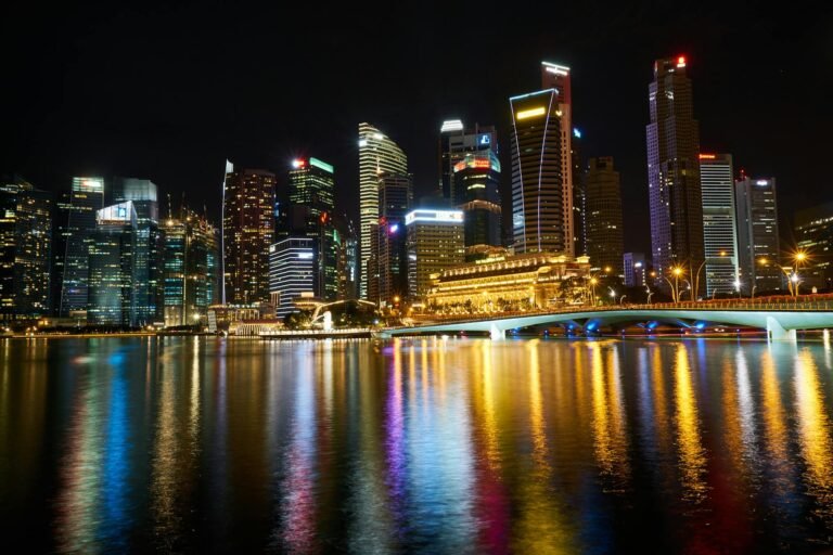 Night view of Singapore skyline reflected over Marina Bay with illuminated skyscrapers and vibrant lights.