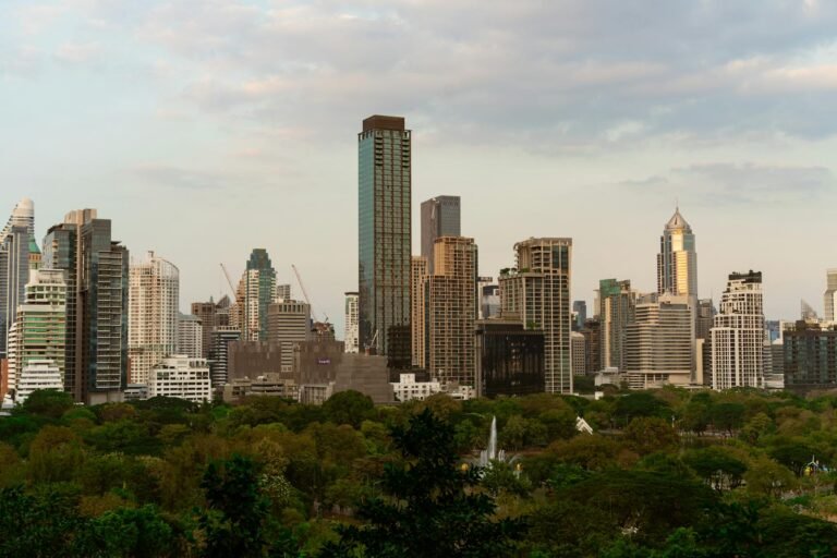 Explore the vibrant skyline of Bangkok with modern skyscrapers at dusk, featuring lush greenery in the foreground.