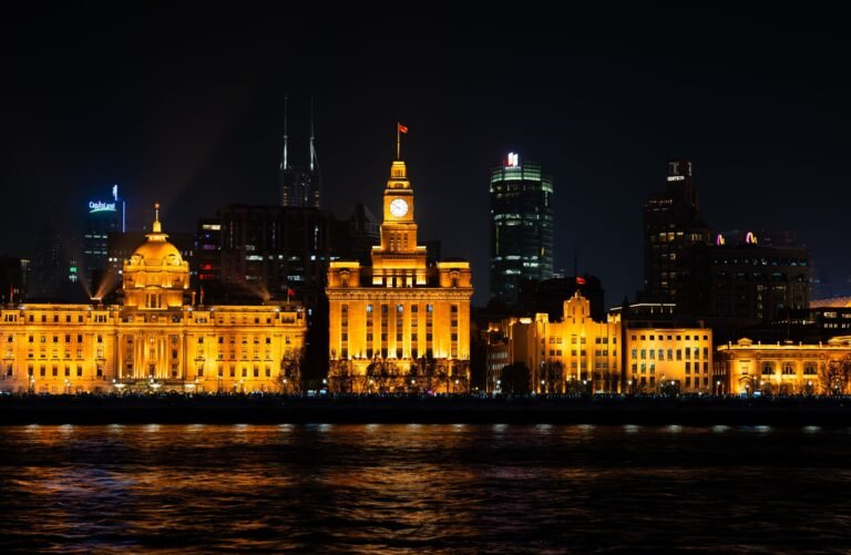 Dramatic night view of Shanghai Bund with illuminated buildings reflecting on water.