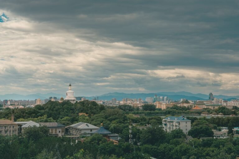 Panoramic view of Beijing with the iconic White Dagoba stupa under a cloudy sky.