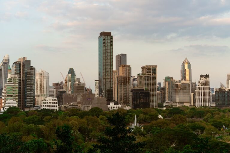 Explore the vibrant skyline of Bangkok with modern skyscrapers at dusk, featuring lush greenery in the foreground.